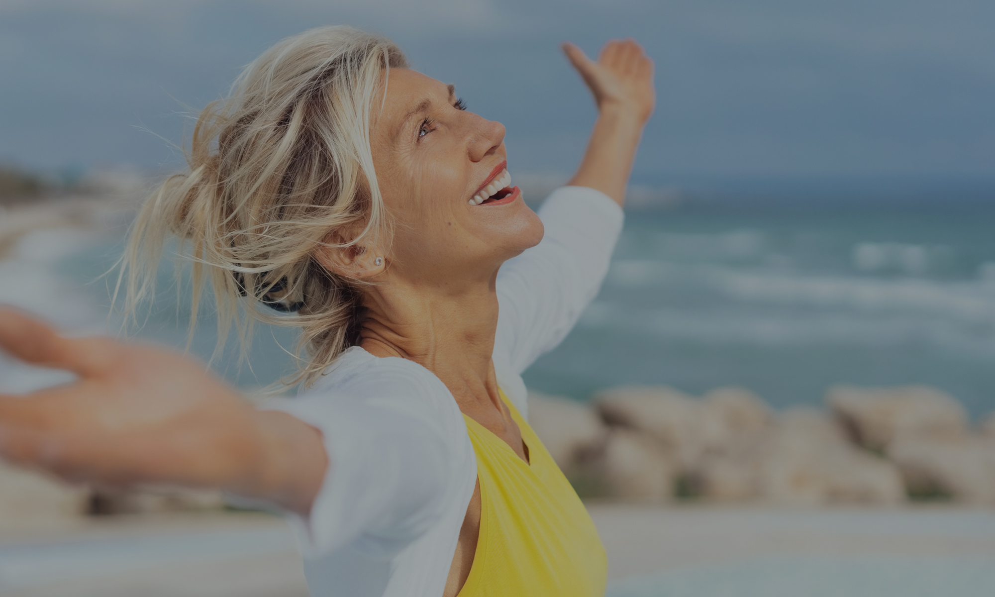 A smiling woman with arms outstretched by the ocean